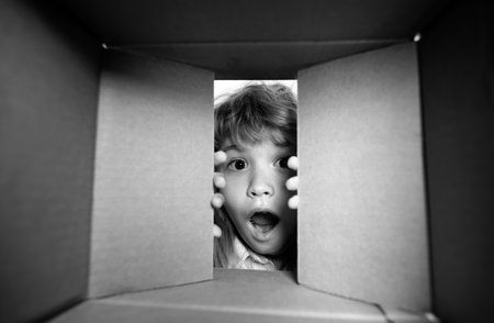 Kid opening package. Child boy age 6 year opening a carton box and looking inside, unpacking concept, surprise unboxing.の写真素材