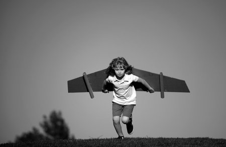 Child playing with cardboard toy wings in the park. Concept of children day. Kid boy in an pilot costume is playing and dreaming of becoming a aviator spaceman. Kids freedom concept.の写真素材