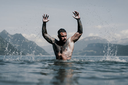 Sexy naked muscular Hispanic man splashing water in lake. Attractive male sexy model in water. Handsome boy rest in Alps lake water. Sexy man naked torso in water. Man freedom lifestyle. Strong muscles guy.の写真素材