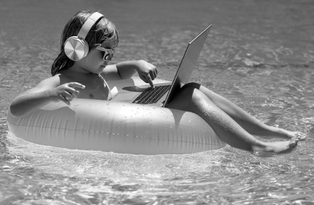 Online working and relax in pool. Child working on laptop computer at poolside swimming pool. Summer online technology.の写真素材