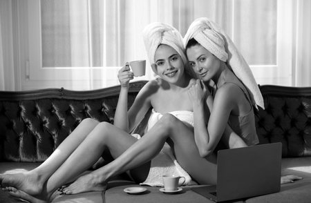 Cheerful ladies drinking coffee, bedroom interior. Female girls friends enjoying morning day at home together, lying on bed and relaxing. Morning girls talking.の写真素材