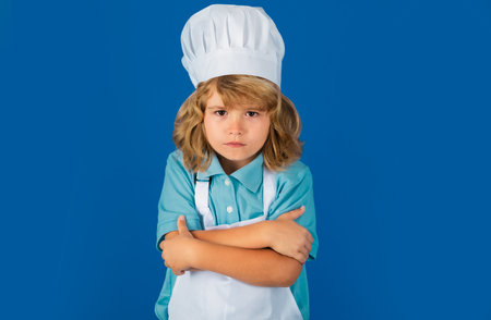 Portrait of a 7, 8 years old child in cook cap and apron making fruit salad and cooking food in kitchen. Cute little blonde happy smiling chef.の写真素材