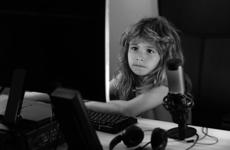 Little kid using desktop pc by night, child boy illuminated by the blue light of a computer screen. Gamer play desktop computer game. Gaming stream and blogging for kids. Social media for kids.の写真素材