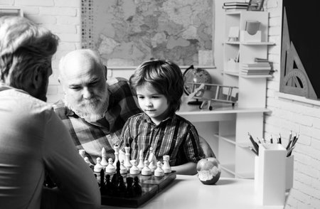 Fathers day. Grandfather father and son playing chess, men generation. Three different generations ages grandfather father and child son study together in home classroom.の写真素材