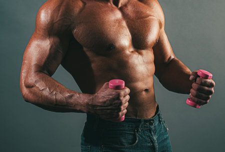 Muscular sexy fitness male body. Man posing shirtless on gray background. Athletic young man with naked torso with dumbbells. Strength and motivation gay concept. Fitness with small dumbbells.の写真素材