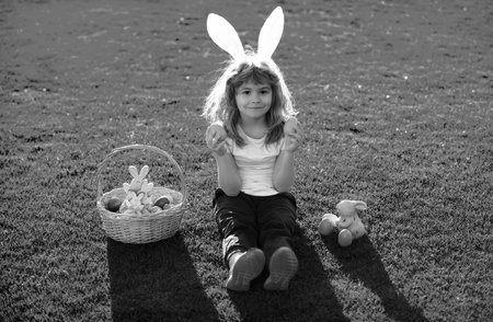 Child with easter eggs and bunny ears laying on grass. Happy Easter kids face. Kids in bunny ears on...