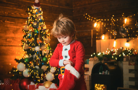 Kid boy santa hold christmas gift red sock. Childhood moments. Christmas stocking concept. Child cheerful face got gift in christmas sock. Check contents of christmas stocking. Joy and happinessの写真素材