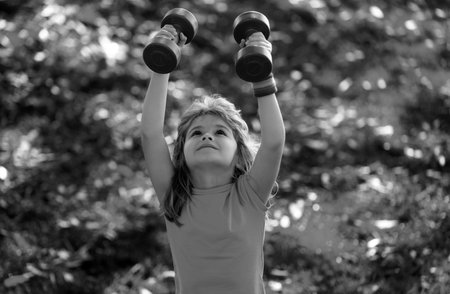 Healthy kid boy with dumbbell exercise outdoor. Little child practice dumbbells exercises in park. Funny excited child sportsman.の写真素材