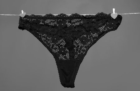 Womans erotic black underwear panties hanging on rope isolated on green background. Lace lingerie, woman underwear.の写真素材