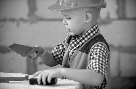 Preschool boy trying to saw, Child sawing on a construction site near house wall. Blond child with...