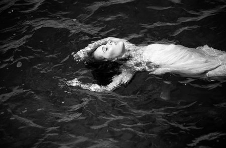 Young woman floating in ocean or sea water, relaxing and taking care of herself. Fashion portrait of graceful cute girl in summer dress during holidays on luxury resort.の写真素材