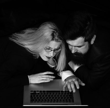 Portrait of a business couple looking at laptop together at dark office.の写真素材