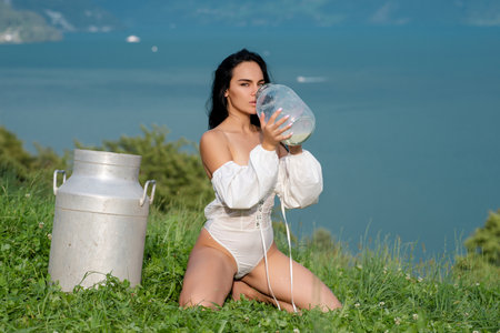 Country Girl with a bottle of fresh milk in the village. Switzerland. Young woman in lingerie drinking milk. Young woman drinking milk from bottle. Beauty romantic girl drink milk outdoors.の写真素材