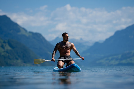Man on paddle board in Alps lake mountains. Leisure activities with paddle on Lake in Switzerland. Man paddle surfing board on Geneva Lake. Muscular sexy strong Hispanic man paddle board surfers.の写真素材
