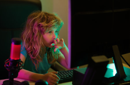 Child playing computer games or studying on pc computer. Kid gamer on night neon lighting. Child using computer technology in home.の写真素材