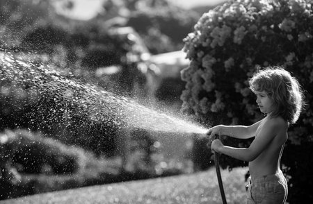 Kids play with water garden hose in yard. Outdoor children summer fun. Little boy playing with water hose in backyard. Party game for children. Healthy activity for hot sunny day.の写真素材
