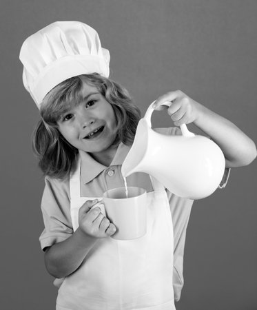 Portrait of a 7, 8 years old child in cook cap and apron making fruit salad and cooking food in...