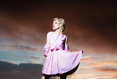 Pinup style woman in summer dress on dramatic sky. Fashion outdoor photo of gorgeous sensual woman in elegant dress clothes. Beauty and fashion girl.の写真素材