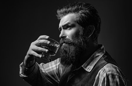 Man Bartender with beard holds glass brandy. Sommelier tastes expensive alcohol drink.の写真素材