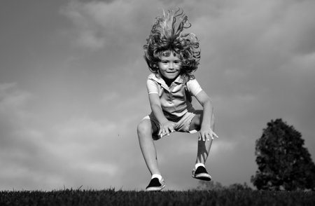 Funny redhead boy playing on the green grass in park, happy childhood. Kids active lifestyle outdoors.の写真素材