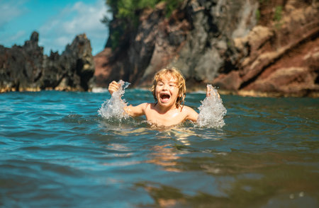 Child playing in ocean water. Kid jumping in the sea waves. Kids vacation on beach. Little excited boy swimming during summer holiday.の写真素材