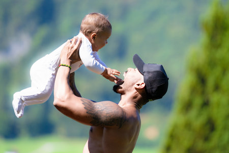 Close up portrait of afro american father kissing multiracial Biracial baby. Father hug Biracial child oudoor. Father with Biracial baby on nature. Hathers hand carrying Biracial baby.の写真素材