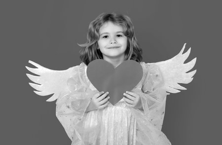 Angel child with heart. Cute angel child, studio portrait. Angel kid with angels wings, isolated...