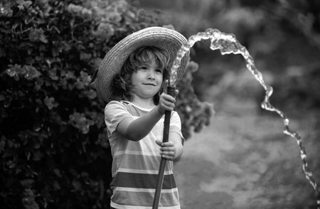 Happy little boy having fun in domestic garden. Child hold watering garden hose. Active outdoors...