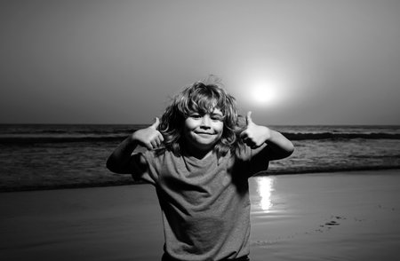 Kid boy on sunset beach, thumbs up. Amazed surprised kids emotions.の写真素材