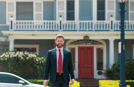 Busines sman standing outside a modern house. Real estate concept. Agent ready to sell home.の写真素材