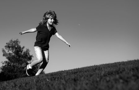 Cheerful boy running on the green grass. Happy child playing in green spring field against sky background. Freedom, active kids healthy outdoor. Fun activity.の写真素材