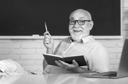 Smiling senior teacher teaching in the classroom on chalkboard. Teacher at university. Man senior...