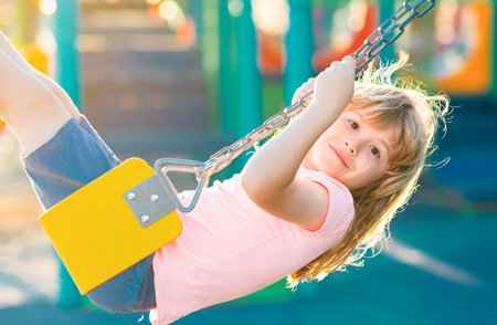 Child swinging on the playground. Cute little kid boy funny while playing on the playground. Summer, childhood, leisure and children concept.の写真素材