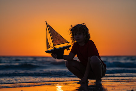 Silhouette of kid playing with toy seailing boat on sunset sea. Dream of summer. Kid play on the...