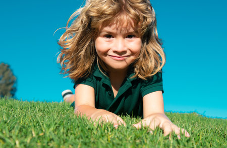Portraits of happy kids playing and laying on grass outdoors in summer park. Funny child face outdoor.の写真素材