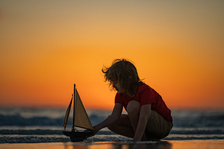 Kid playing on the beach. Child play on the sea with toy ship boat. Little child having a happy...