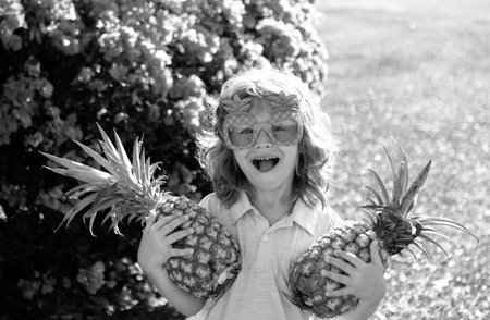 Child wearing funny sunglasses with pineapple. Kid with tropical fruit. Exotic vacation. Fruit for children. Summer kids holiday.の写真素材