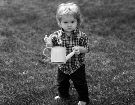 Cute little boy child watering flowers with watering can. Lifestyle portrait baby child in happines at the outside in the meadow.の写真素材