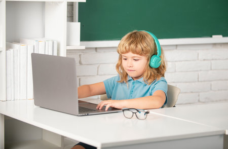 Genius child programming. Child boy in headphones using a laptop and study online with video call teacher at school.の写真素材