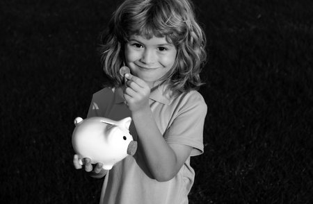 Piggy bank and little boy with coin. Baby child putting a coin into a moneybox piggy bank, kid saving money for future concept.の写真素材
