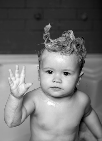 Washing adorable baby in bathroom. Kid with soap suds on hair taking bath. Closeup portrait of smiling kid, health care and kids hygiene. Kid bathing in bathroom.の写真素材