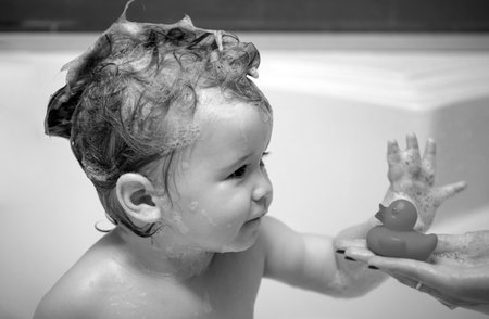 Baby child washing in a bathroom in foam. Child bubble bath. Smiling kid in bathroom with toy duck.の写真素材