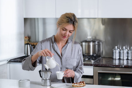 Young woman have breakfast, pouring milk in coffee. Woman at home in morning. Beautiful sensual female housewife in sexy pajama in kitchen cooking breakfast.の写真素材