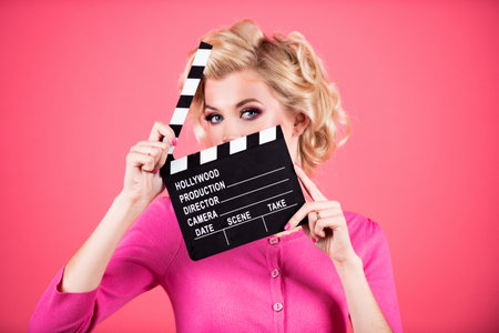 Women eyes through clapper board. Movie production clapper board, film. Clapperboard film industry. Pretty girl holding clapper board shocked hiding behind clapper board isolated on studio background.の写真素材