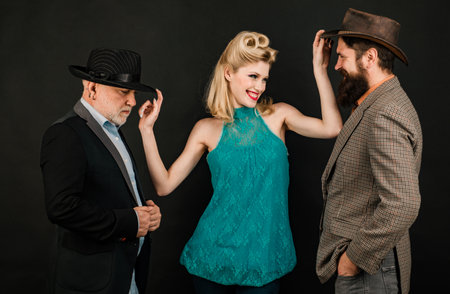 Mature stylish senior man and berded guy with funny yong woman wear retro hat, modern and hipster or vintage style for people. Young vs old generation.の写真素材