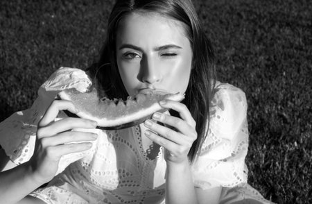 Portrait of happy woman enjoying summer and eat watermelon in park. Youth girl about biting wedge of juicy watermelon enjoying summer.の写真素材