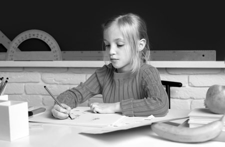 Portrait of cute little schoolgirl writing in book with classmates in background at classroom. Girl...