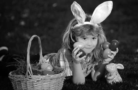 Child boy hunting easter eggs in spring lawn laying on grass. Child bunny boy with rabbit bunny ears.の写真素材
