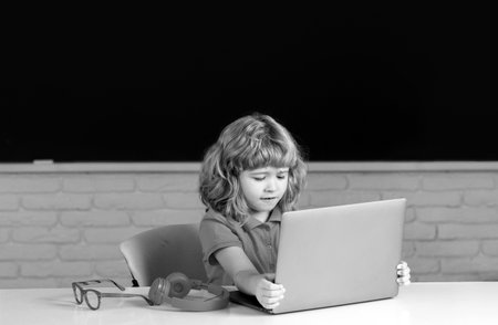 Kid boy learning lesson at school, making homework and using notebook gadget.