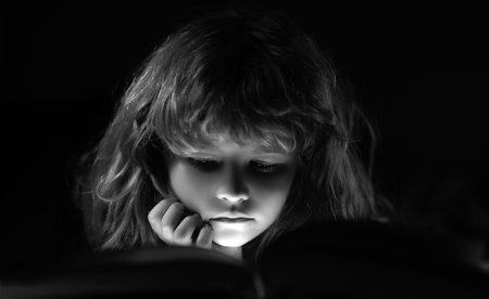 Close up face of child reading a magic book in bed. Kid boy read books at home.の写真素材